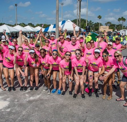 Group of athletic women and men in hot pink t-shirts on a sunny day at outdoor event