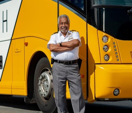 Smiling Motorcoach Operator stands beside a yellow and white Mears coach bus.