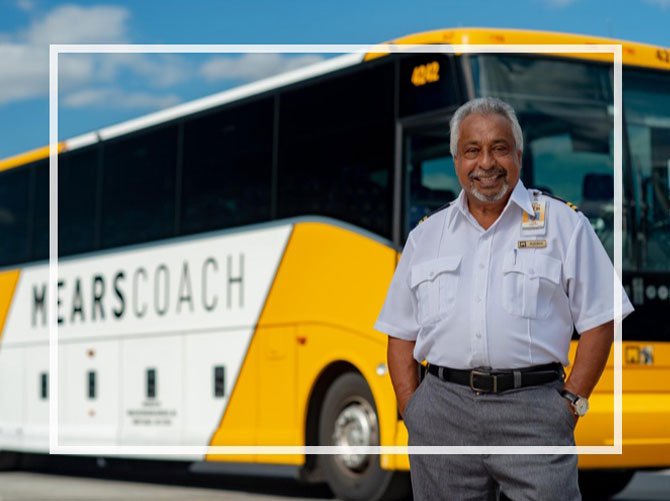 Smiling Motorcoach Operator stands beside a yellow and white Mears coach bus