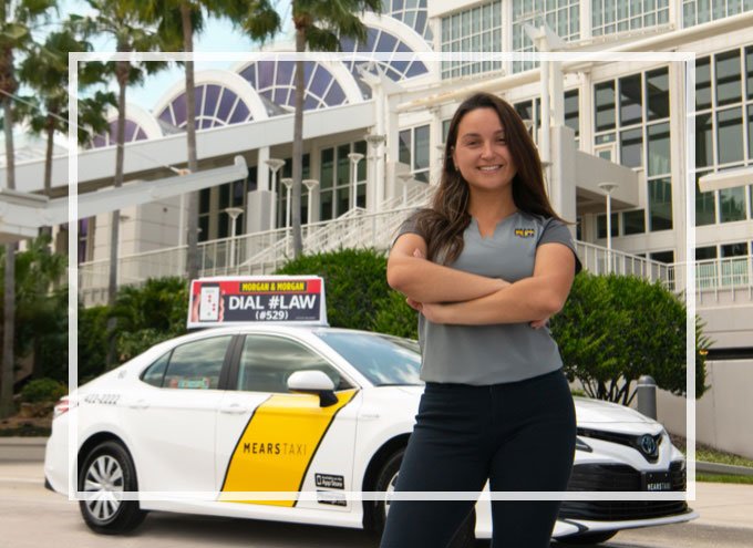 Happy taxi driver stands beside a white and yellow Mears Taxi outside the Orlando Convention Center